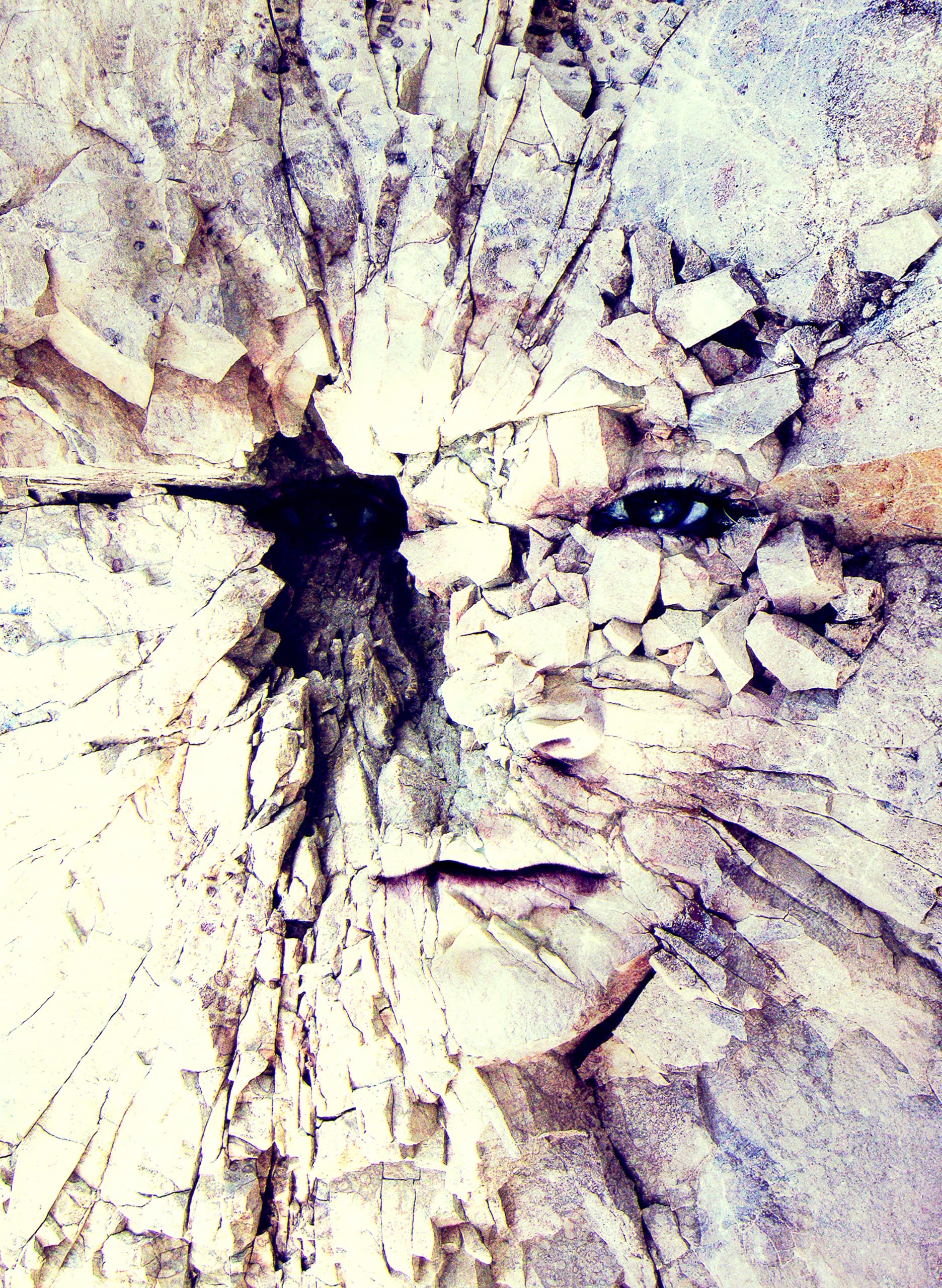 A surreal image of a human face embedded in a cracked stone surface. The eyes and lips are smoothly integrated into the fragmented texture, creating an illusion of the face emerging from the fissures. The colors are earthy tones, with light highlighting the contours.