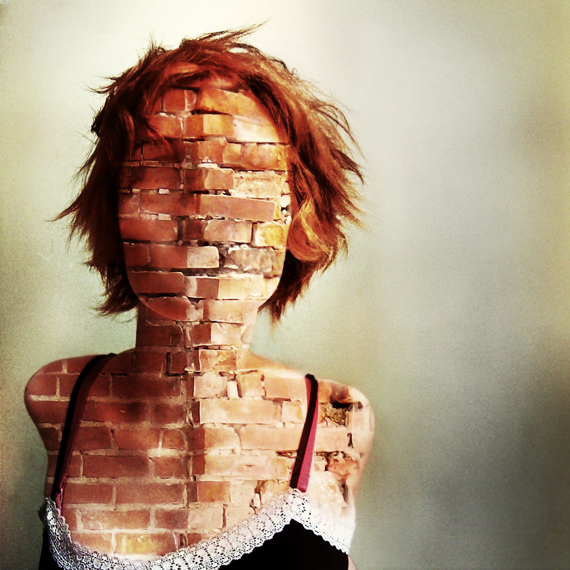 A woman with red hair is depicted with her face and upper body made of brick, blending into the background. She is wearing a black and white lace-trimmed tank top with red straps against a neutral backdrop, creating a surreal and striking visual that reflects the complexity of our jaded world.