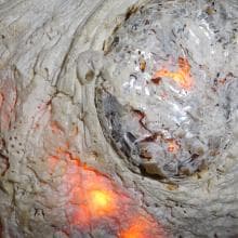 Close-up of a textured surface resembling coral or rock, with intricate patterns and crevices. Bright, warm orange lights glow from within, casting a fiery reflection. The overall appearance suggests a blend of natural and abstract elements, merging the organic with the luminous.