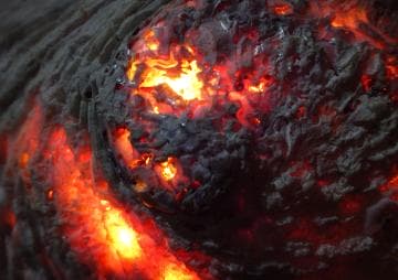 Close-up of smoldering coals, glowing with intense orange and red hues. The charred surface displays intricate textures and patterns, with bright embers illuminating the scene, creating a contrast against the darker, ashy areas surrounding the glowing sections.