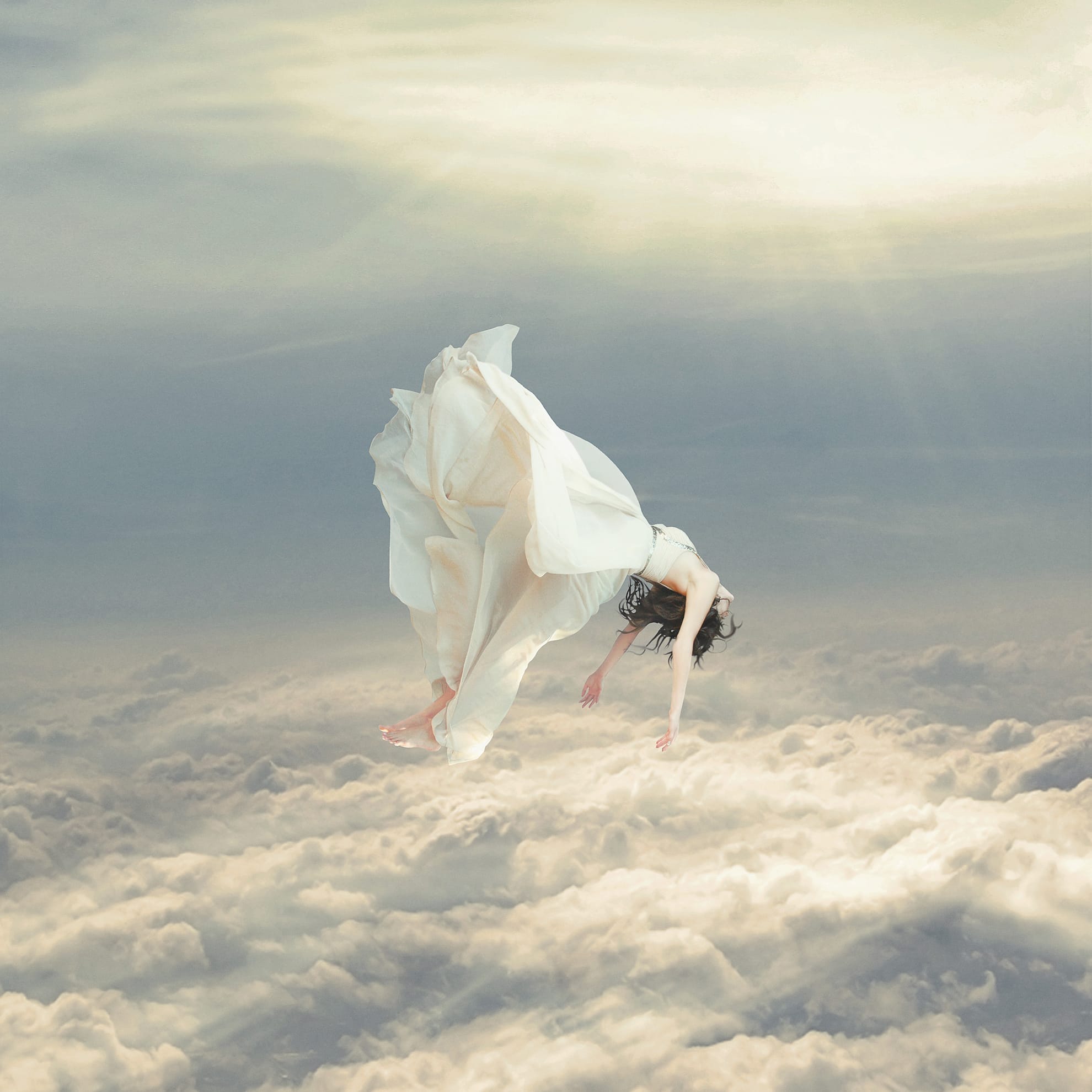 A woman in a flowing white dress appears to float effortlessly above a sea of clouds, evoking the sensation of a free falling dream. Horizontally positioned, her arms hang down and her head tilts back, creating a serene and dreamlike atmosphere. Sunlight filters through the clouds, illuminating the scene with a soft glow.
