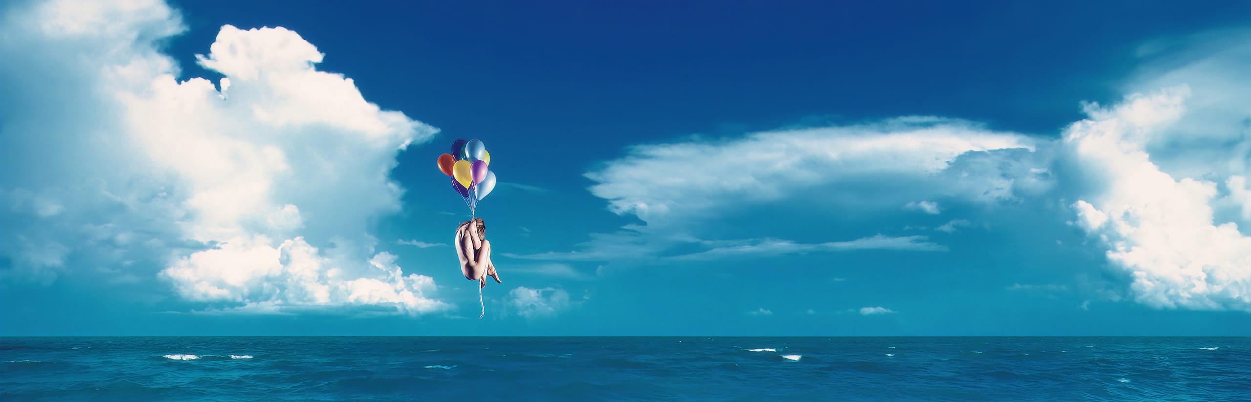 A person is floating above the ocean, grasping a bundle of colorful balloons. The sky is clear with a few fluffy clouds scattered. The deep blue sea below has gentle waves, and despite the whimsical impression of flying freely, an undercurrent of infinite sadness subtly tinges the scene.