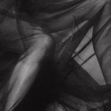 Monochrome image from the Presence Series featuring a translucent, flowing black fabric draped over a person's bare leg and arm. The ethereal texture creates a ghostly, abstract effect, with light and shadow interplay adding depth and contrast to the 10/10 scene.
