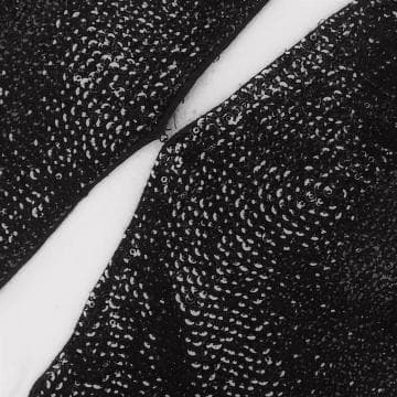 Close-up of two sections of black, glittery fabric with sequins from the Presence Series, separated by a slim, diagonal strip of white. The sequined surfaces shine under the light, creating a textured and sparkly appearance while the stark white strip provides contrast.