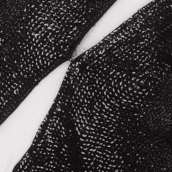 Close-up of two sections of black, glittery fabric with sequins from the Presence Series, separated by a slim, diagonal strip of white. The sequined surfaces shine under the light, creating a textured and sparkly appearance while the stark white strip provides contrast.