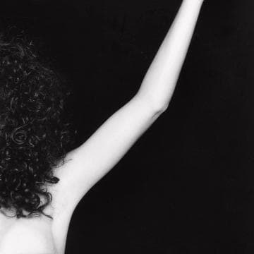 Part of the Presence Series, this black and white image captures a person with curly hair, raised arm, and bare shoulder against a dark background. The arm is bent slightly at the elbow, with the hand out of the frame. The photo excels in highlighting the texture and form of both hair and arm—truly 10/10.