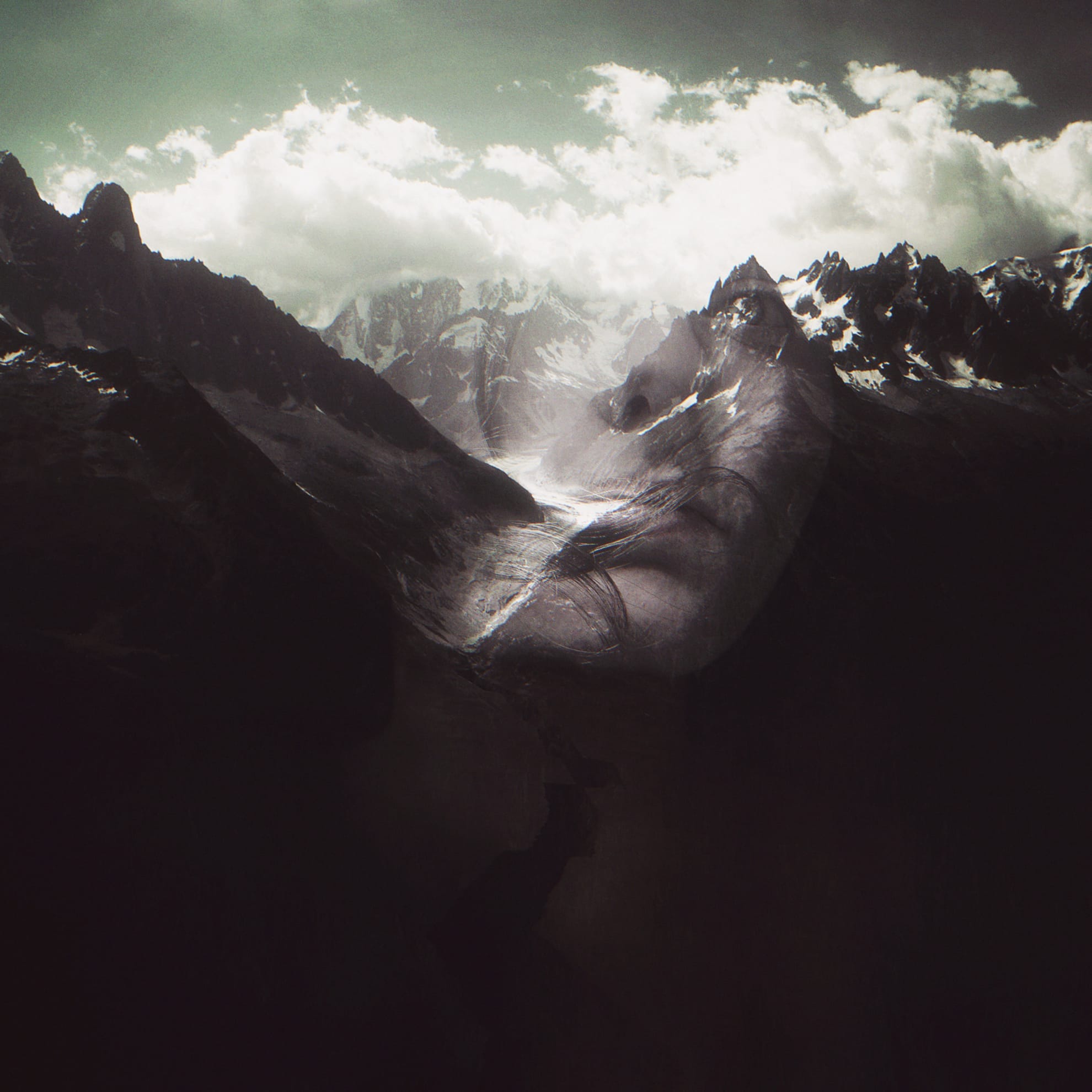 A surreal image of a mountainous landscape with snow-capped peaks and a glacier under a cloudy sky. The scene has a double exposure effect, overlaying a serene human face onto the mountains, blending natural elements with human features for a dreamlike atmosphere.
