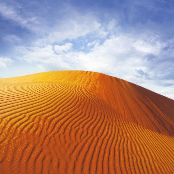 A vast desert landscape features a prominent sand dune under a bright blue sky with scattered clouds. The dune is covered with intricate ripples and patterns created by the wind, showcasing the rich orange and golden hues of the sand contrasting against the sky.