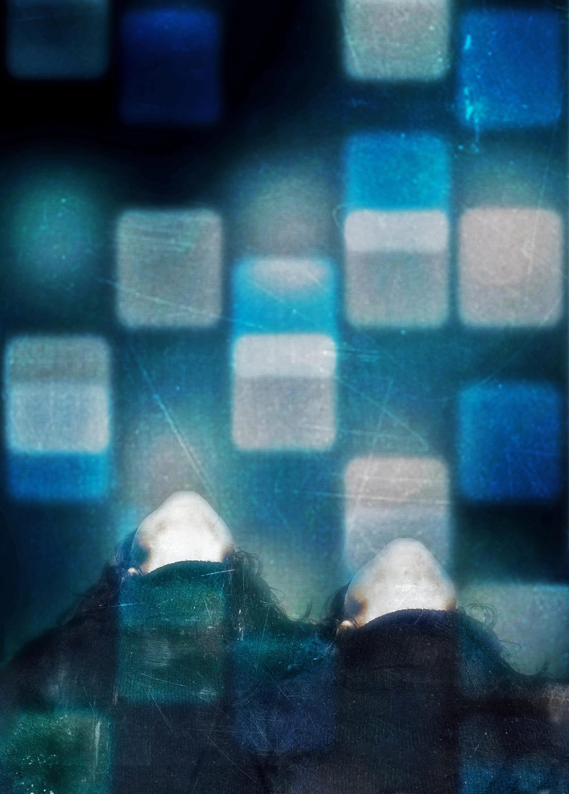 Two individuals lie with their heads tilted back, surrounded by a pattern of illuminated blue and white squares. The scene has a dreamy, surreal ambiance, with soft lighting and blurred edges, creating a sense of depth and ethereal atmosphere.