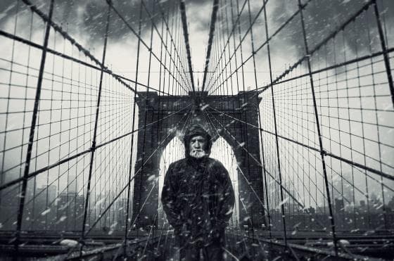 A person stands on the Brooklyn Bridge during a snowy day. The scene is in black and white, creating a dramatic and moody atmosphere. The geometric lines of the bridge's cables converge towards the figure in the center, who is dressed in a dark winter coat and hat. Snowflakes are visible in the air.