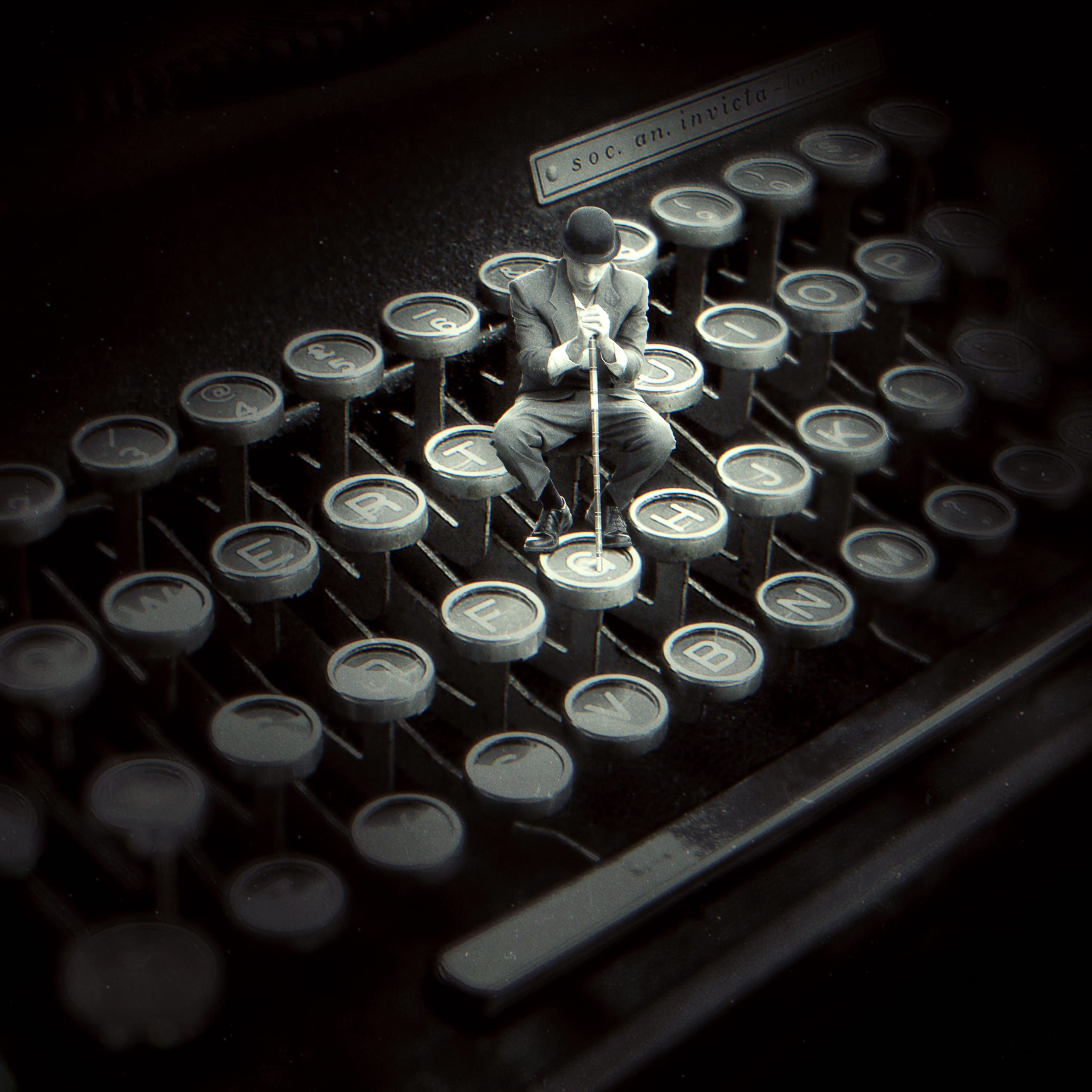 A miniature man in a suit and bowler hat sits on the key of an old typewriter. The keys appear disproportionately large, emphasizing his small size. The image has a vintage, monochromatic tone, blending surrealism with nostalgia.