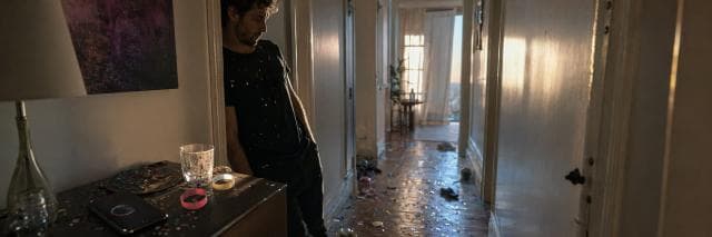 A man stands in a hallway with confetti and party items scattered on the floor and table, showing resilience after the celebration.