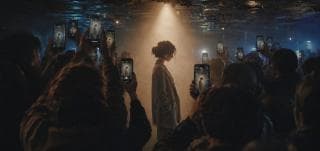 A person stands confidently as a crowd gathers around, taking photos with their phones.