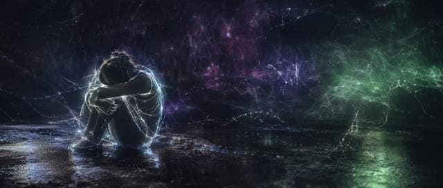 A person sits on the ground hugging their knees, surrounded by glowing colors in a chaotic, dark space.