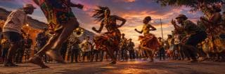 People dance barefoot in colorful clothes at sunset, surrounded by musicians and onlookers under a vibrant sky.