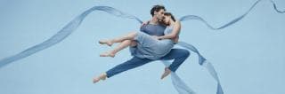 Two dancers in blue leap with swirling ribbons, showcasing a surreal display of strength and spirit.