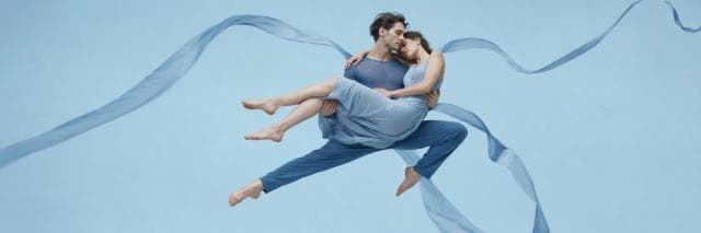 Two dancers in blue leap with swirling ribbons, showcasing a surreal display of strength and spirit.