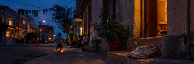 A single sneaker rests on a stoop by a doorway as a child runs down a quiet street.