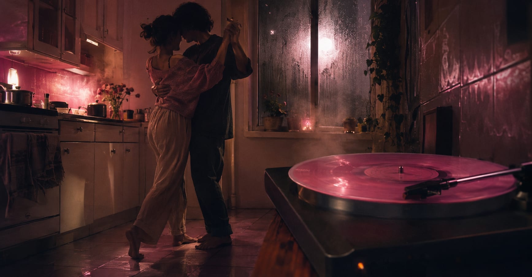 A couple dances energetically in a kitchen while rain falls outside, warm pink light illuminating the area near a record player.