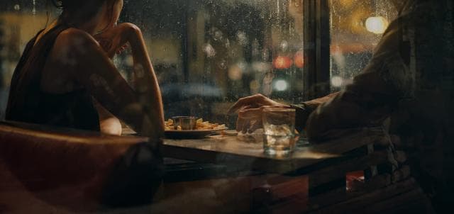 Two people share fries at a table by a rainy window in a quiet restaurant.