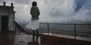 Person in a white dress stands on a wet rooftop, looking over a fantastical cityscape under stormy skies.